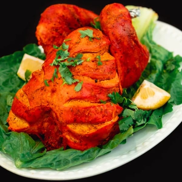 Zaffron's vibrant red tandoori chicken, garnished with fresh cilantro and lemon wedges on a bed of lettuce.