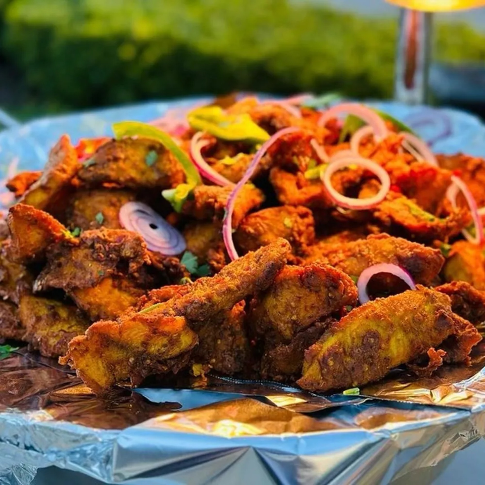 Close-up of Zaffron's fried Afghan potatoes with red onions and green peppers on foil.