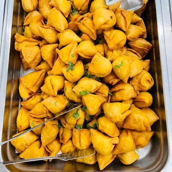 A metal tray filled with golden-brown, triangular Afghan samosas, garnished with fresh herbs, and serving tongs.